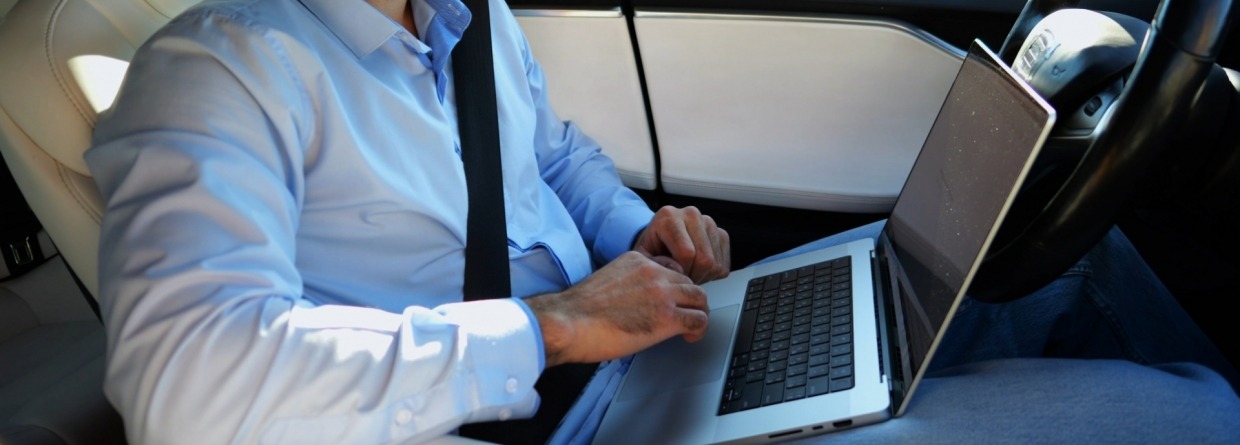 Zakenman met laptop op schoot rijdt in een auto